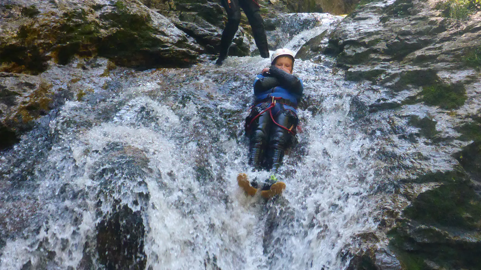 Eine junger Canyonaut, der einen Wasserfall hinunterrutscht.