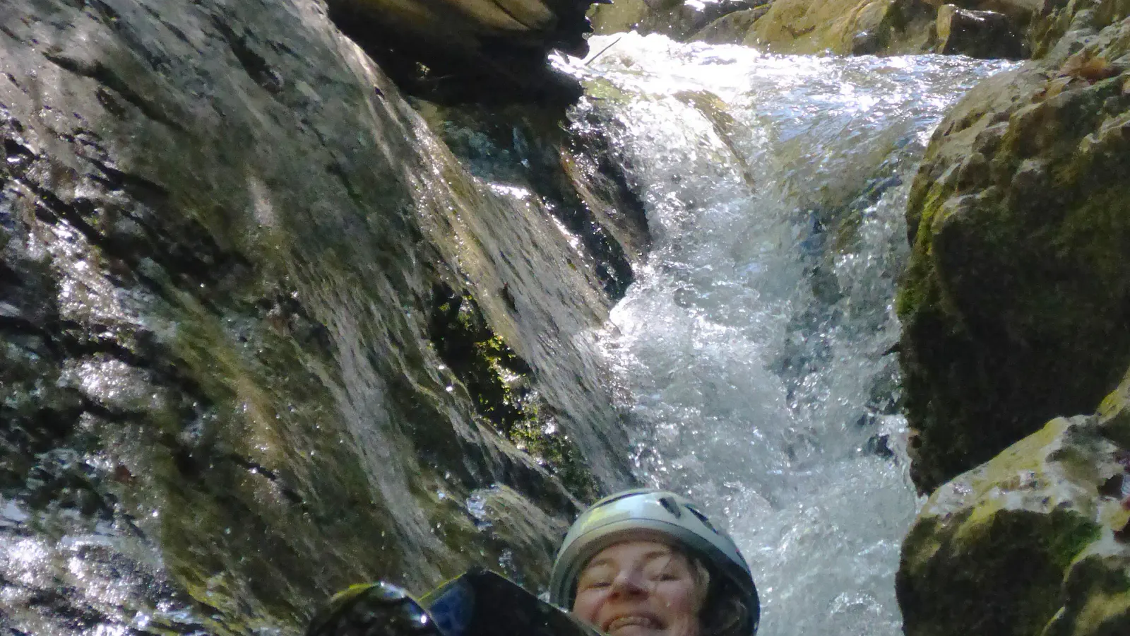 Eine Person lässt sich durch schäumendes Wasser in einer Schlucht treiben, ein Wasserfall im Hintergrund.