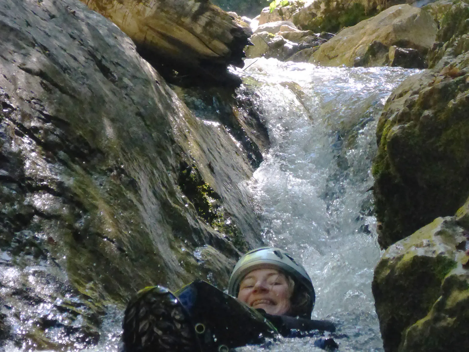Eine Person lässt sich durch schäumendes Wasser in einer Schlucht treiben, ein Wasserfall im Hintergrund.