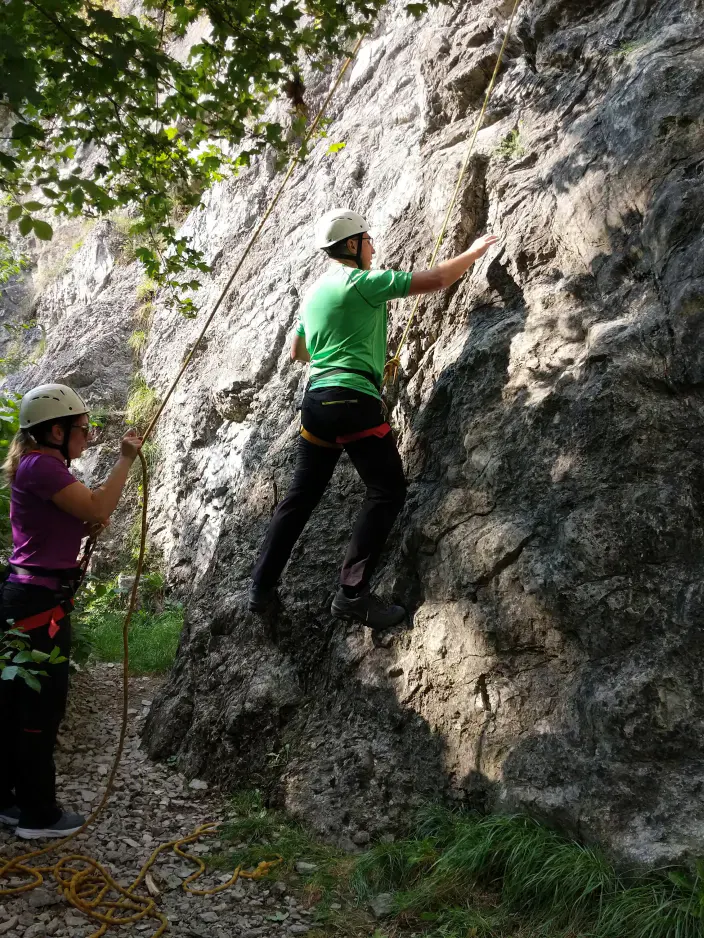 Eine Person beginnt eine Route auf einem Felsen zu klettern während eine andere Person sie sichert.