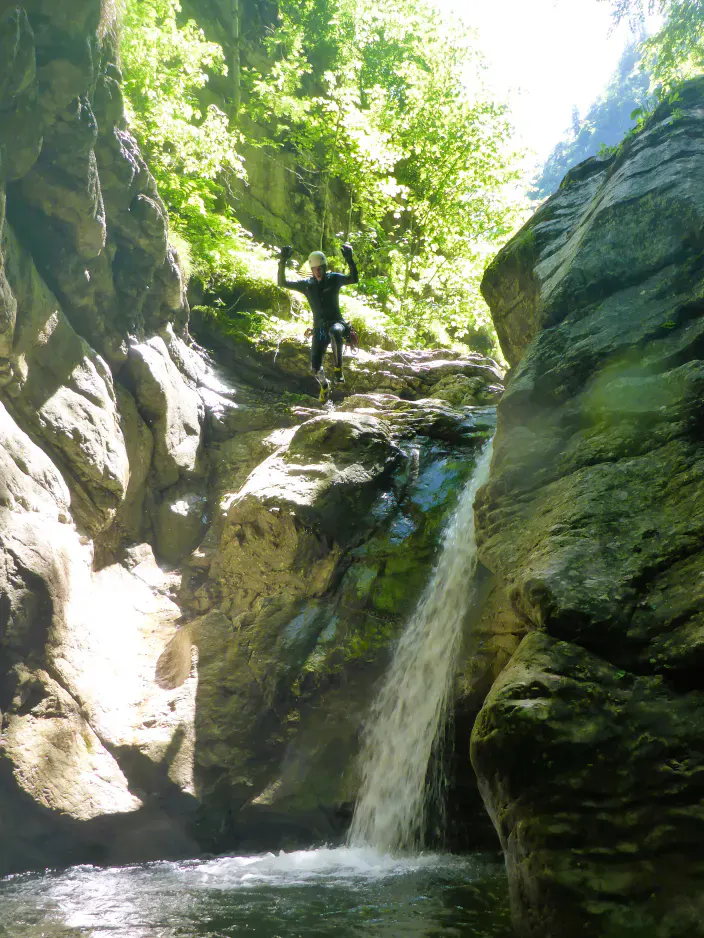 Ein Canyonaut springt mit einem Wasserfall im Hintergrund ins Wasser.