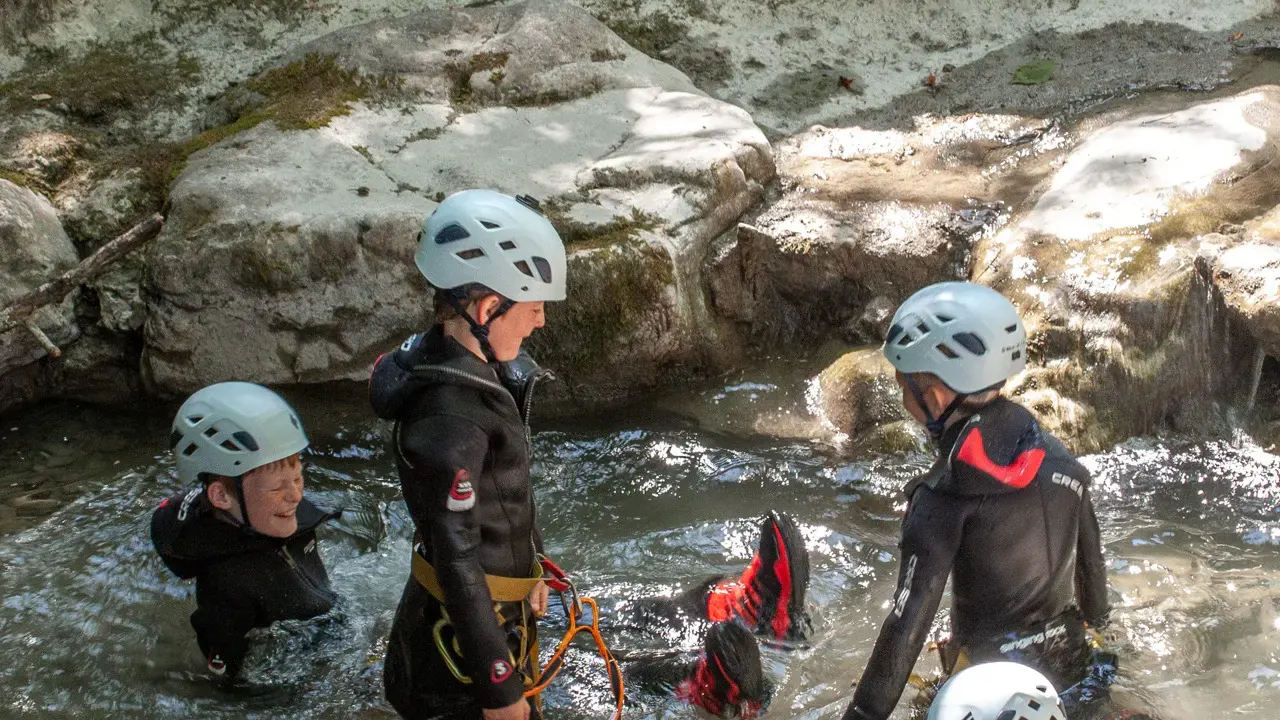 Kinder sitzen & stehen in Canyoningausrüstung im Bach