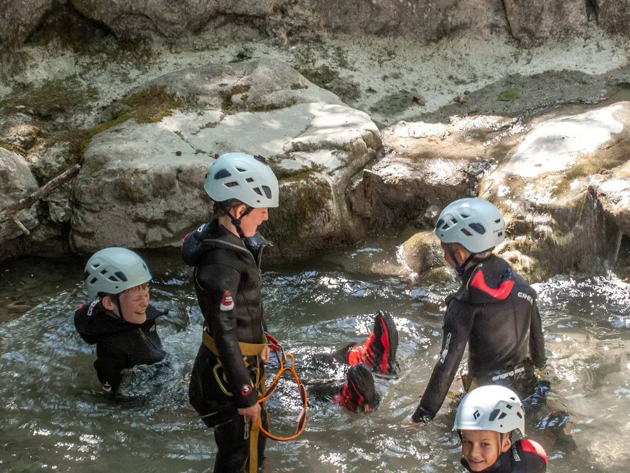 Kinder sitzen & stehen in Canyoningausrüstung im Bach