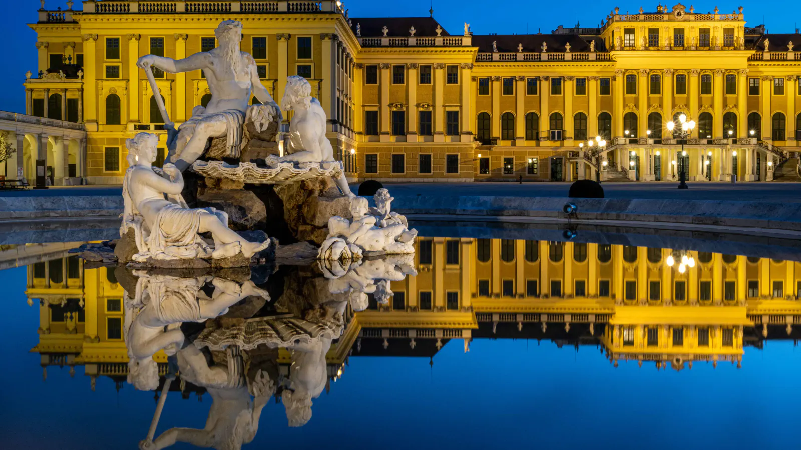 Beleuchtetes Schloss Schönbrunn mit Spiegelung im Wasser bei Nacht.