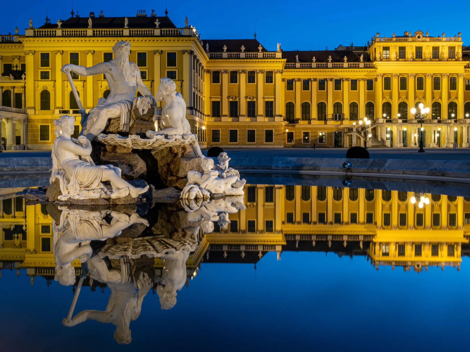 Beleuchtetes Schloss Schönbrunn mit Spiegelung im Wasser bei Nacht.