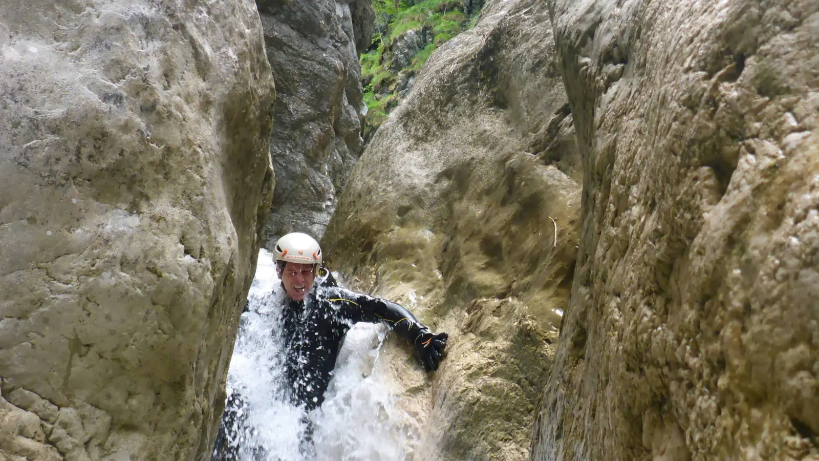 Eine Person rutscht in einer engen Schlucht durch schäumendes Wasser.