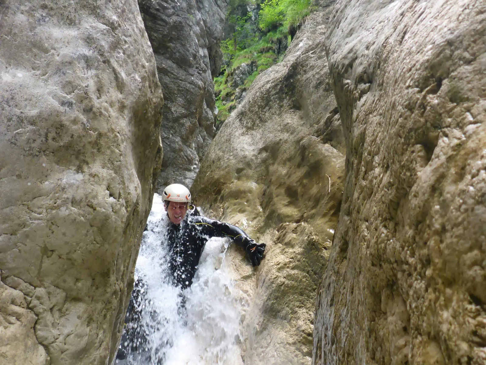 Eine Person rutscht in einer engen Schlucht durch schäumendes Wasser.